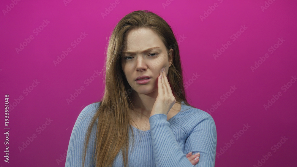 Obraz premium Young caucasian woman with pained expression hand on cheek in pink studio set; discomfort toothache.