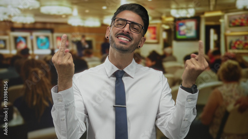 Foto Man wearing glasses and earring with white shirt and tie shows both middle fingers in building; defiance