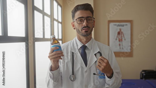 Obraz na płótnie Young hispanic man doctor holding medicine bottle and stethoscope in clinic building; empathy compassion trust