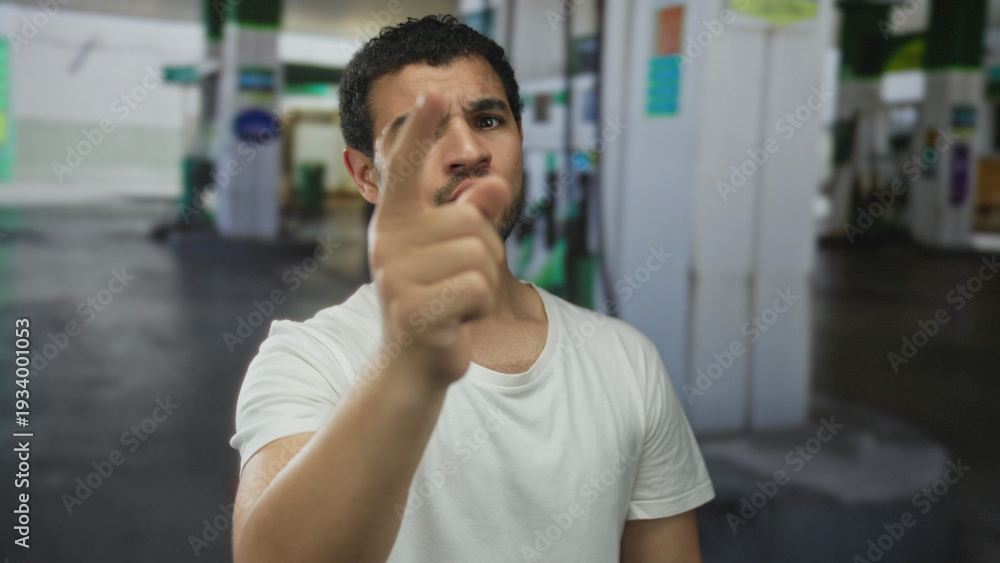 Naklejka premium Man in white shirt frowns and extends hand gesture toward petrol pump at building; invitation greeting.