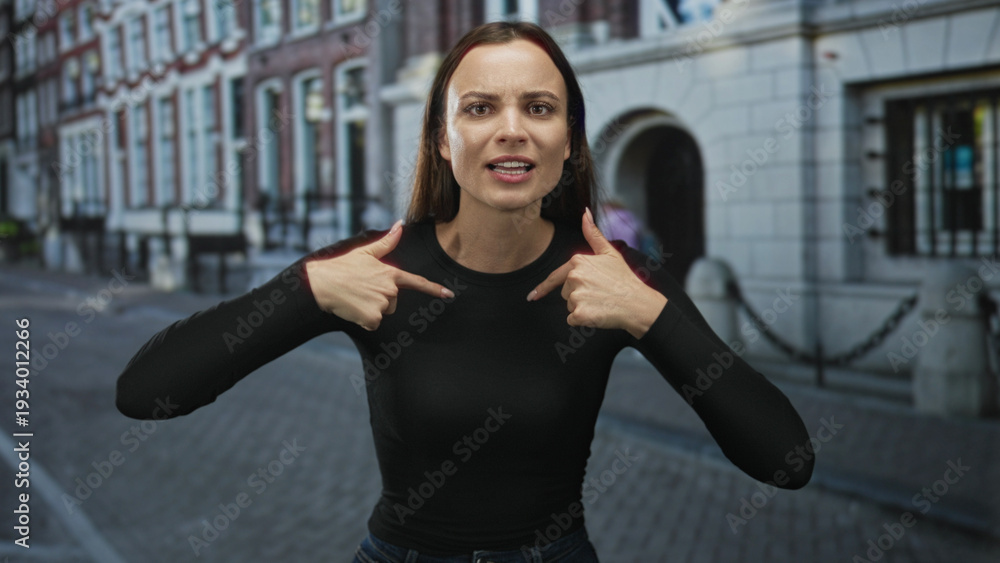 Obraz premium Young woman waving hands and speaking with raised hands on cobblestone street by building facade; frustration.