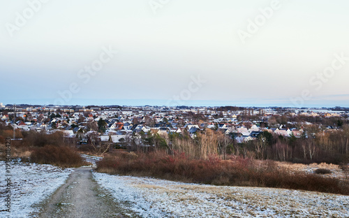 Winter view over Bunkeflostrand, a rich, growing residential suburb or neighbourhood in Malmö, Sweden, with snow-dusted houses and a path leading down from a hill. Malmo housing issues concept