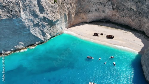 Aerial drone view of famous Navagio Shipwreck Beach with turquoise sea water and boats in Zakynthos island, Greece on a bright sunny da