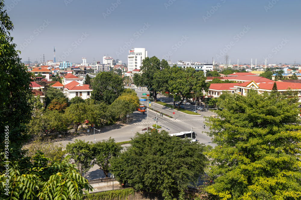Obraz premium High-angle view of a vibrant Hoa Lu Old town, , Ninh Binh, Vietnam, capturing daily urban life with cars, buses, and buildings amidst green trees.