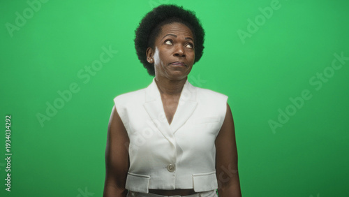 Obraz na płótnie Woman in white sleeveless vest with eyes closed and pursed lips standing before a green screen in a studio, showing subtle head tilt and still posture; skepticism