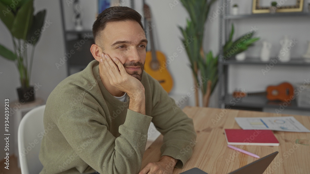 Fototapeta premium Young man thinking in cozy living room with guitar and plants surrounding him at home office setup