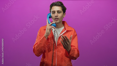 Tableau sur toile Man in orange prisoner jumpsuit holds blue telephone handset to ear and gestures with hand in studio; remorse reflection