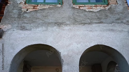 Old rural house facade with green wooden windows and unfinished plaster wall