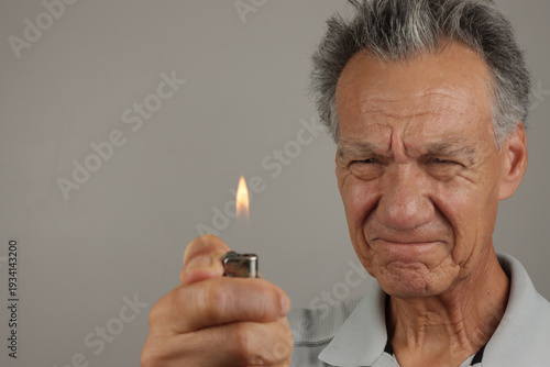 Older Man holding lit butane lighter up close to his face 