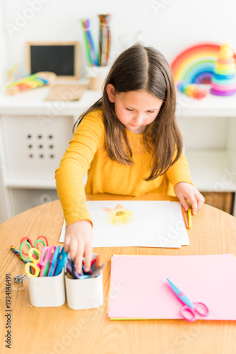 Little girl using crayons to paint while homeschooling wearing a yellow shirt in a bright and colorful home