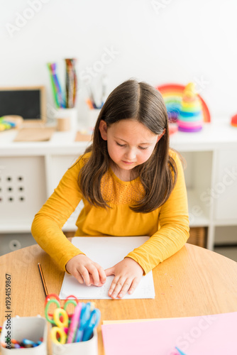 Little girl erasing a math problem while doing her homework on a table in a bright and colorful home