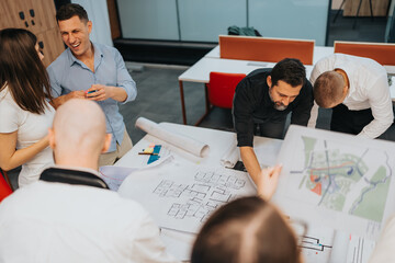 A group of business colleagues gathers around large architectural plans, examining drawings and maps. They collaborate and discuss ideas in a bright, modern office.