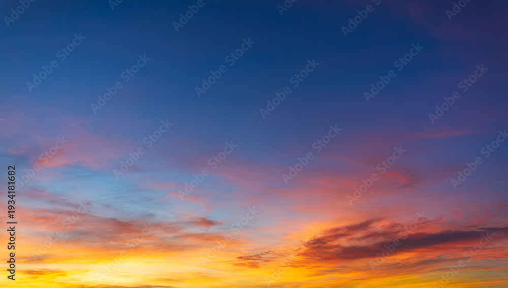 Obraz premium Beautiful panoramic sunset sky with colorful clouds in blue and golden orange hues,A stunning wide-angle shot of a vibrant sunset sky featuring a dramatic blend of fiery orange, soft pink, 