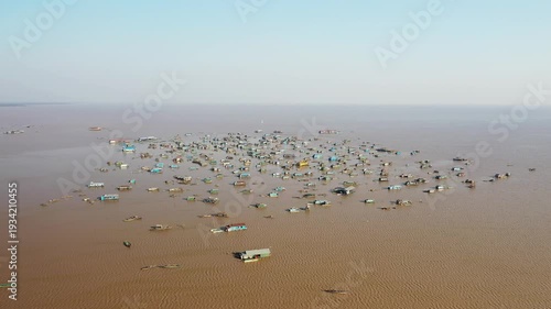 Aerial view of the floating village of Chong Kneas on Tonle Sap Lake, Cambodia, with numerous houses and boats scattered across the water under a clear sky.