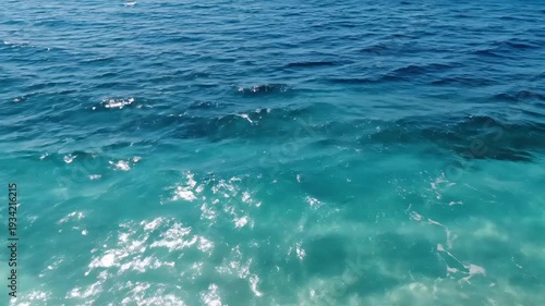 Crystal clear turquoise ocean water with gentle waves and white foam rolling onto a sandy beach under bright sunlight.
