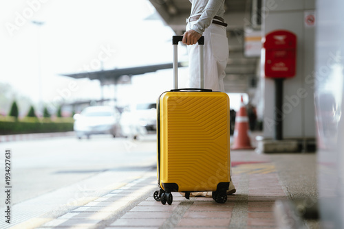 Close-up of traveler pulling yellow suitcase at airport curbside, ready for departure and transportation.
