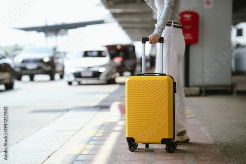 Close-up of traveler pulling yellow suitcase at airport curbside, ready for departure and transportation.