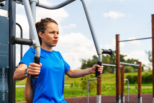 Active woman uses outdoor exercise equipment to exercise in fitness park on a sunny summer day.