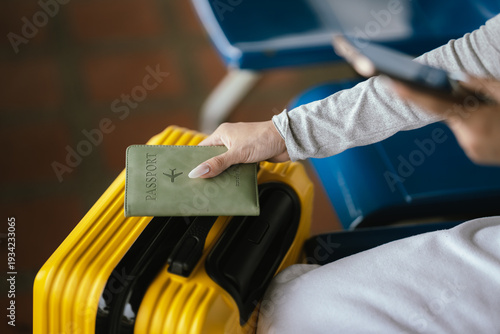 Close-up of traveler holding passport and smartphone on yellow suitcase while waiting at airport terminal, preparing for flight.