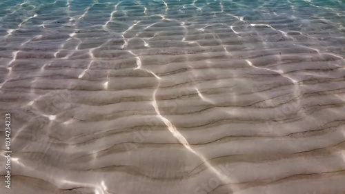 Clear turquoise water ripples over sandy bottom, showcasing the gentle movement of waves and light reflections in a serene coastal environment