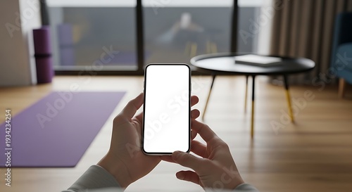 Person holding smartphone with blank screen in modern home interior with yoga mat and coffee table