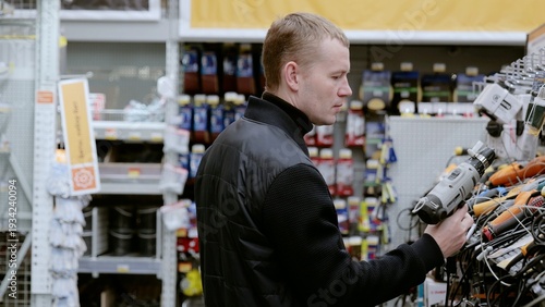 Fotografie Man chooses an electric drill in a hardware store, comparing models on shelves for his diy project