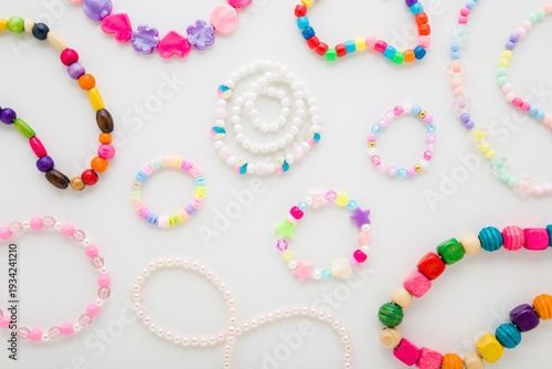 Bracelets and necklaces for little child girl on light gray table background. Created beaded jewellery from colorful different plastic parts. Closeup. Flat lay. Top down view.