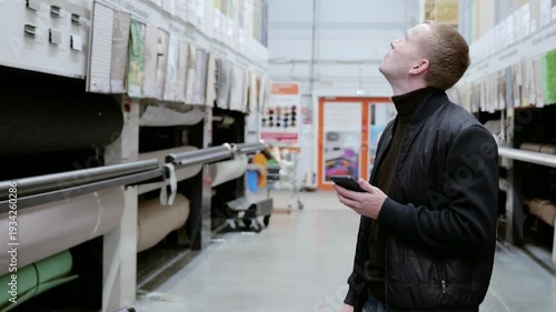 Wallpaper Mural Man using his smartphone is searching for goods and comparing prices in a hardware store. He is holding a smartphone and looking around. Choosing Carpeting at a Home Depot Torontodigital.ca