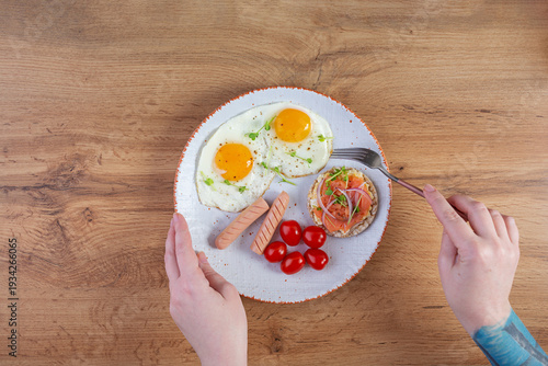 Fried eggs with sausage, cherry tomatoes and buckwheat bread with salmon fish. With hands in the frame