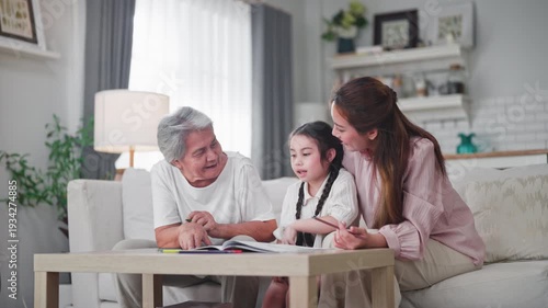 Joyful Asian family of three generations enjoys drawing and coloring together on a wooden table in a bright modern living room at home.