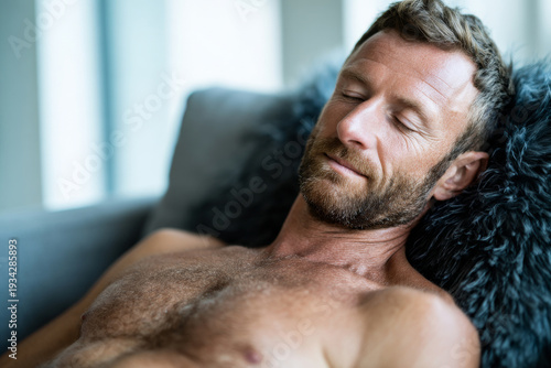 shirtless man dozing on recliner in modern living room, relaxed and serene expression, soft daylight.