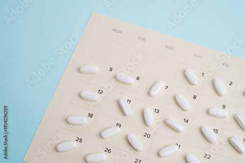 White pills arranged on monthly calendar page on blue background. Medical treatment schedule concept.