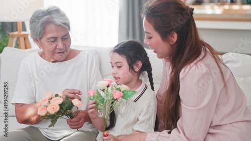 Joyful Asian family of three generations shares a moment of laughter while holding beautiful flowers in a bright modern living room at home.