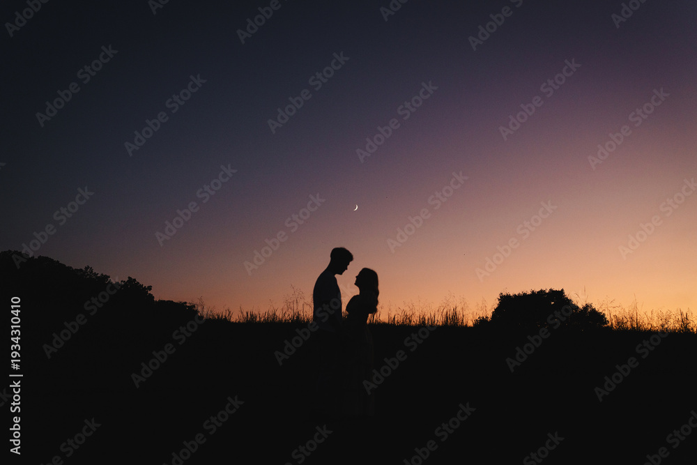 Fototapeta premium Silhouette of romantic couple at sunset under crescent moon
