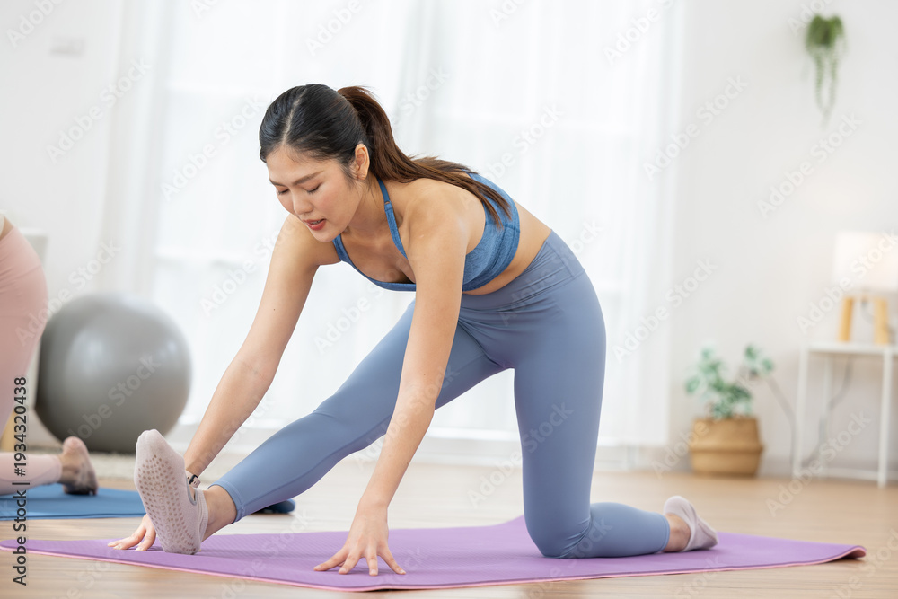 Obraz premium Focused young asian woman stretch leg muscle on yoga mat home feeling determination effort training hard strong healthy body flexible movement workout routine fitness lifestyle