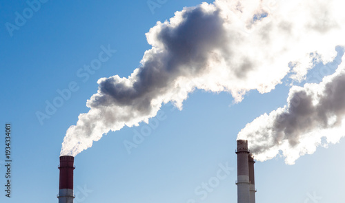CHP emissions. Smoking chimney releasing smoke against a blue sky. Smoke from factory pipe of heat station in the city. Air pollution. Nuclear power plant cooling. CO2, greenhouse gases emissions.