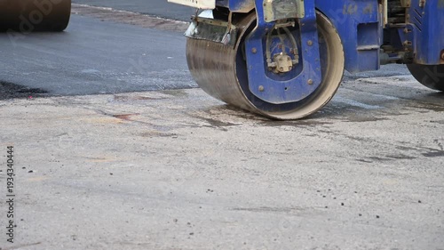 Yellow metal roller vehicle flattening fresh black asphalt on a road construction site.