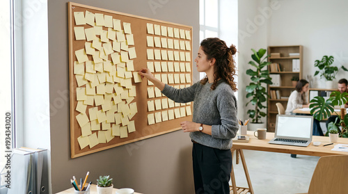 Woman organizing sticky notes on corkboard in modern office for agile workflow planning project management task prioritization and productivity teamwork