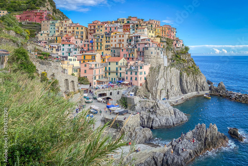 Scenic view of Manarola along Cinque Terre with colorful houses on a rocky coastline above the Mediterranean Sea in Liguria, Italy against blue sky with clouds