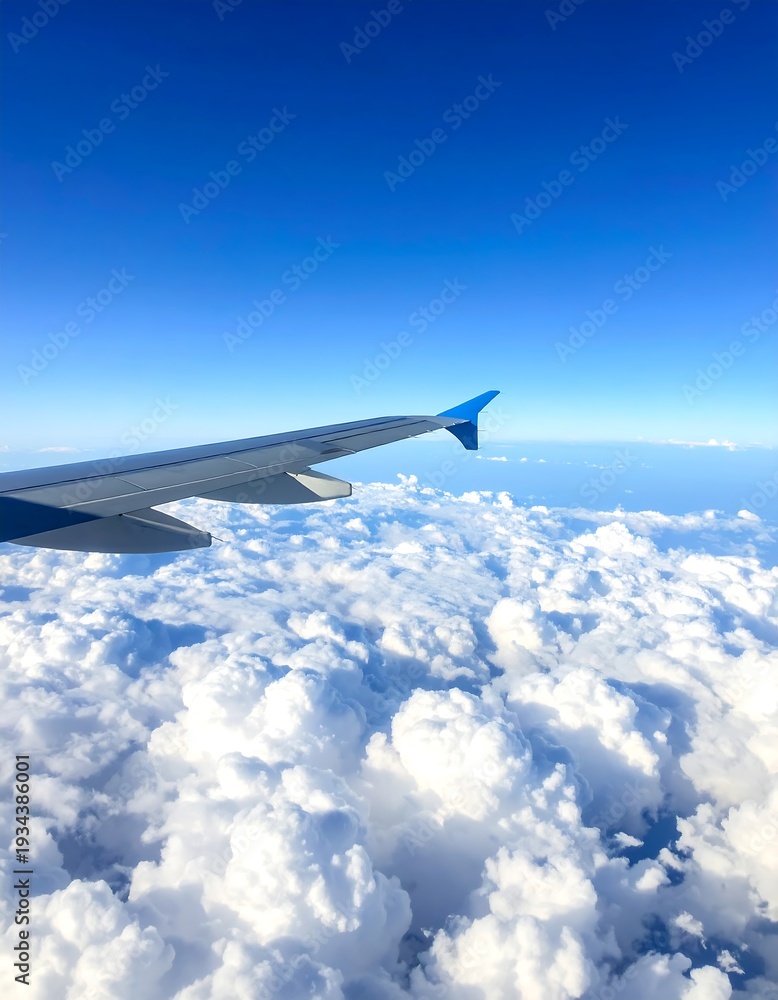 Fototapeta premium Airplane wing in flight above fluffy white clouds under clear blue sky