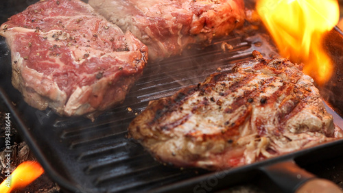 Konstfotografi Thick, juicy steaks sizzling and searing on a cast iron grill pan with flames li