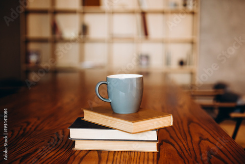 Grey cup on a stack of books on a dark library background, copy space.