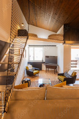 Front view of a living room inside a mountain chalet. The room is split level, with a small guest bedroom upstairs.