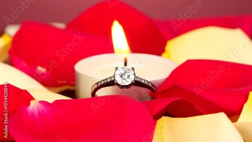 A diamond ring rests amidst vibrant rose petals, illuminated by a soft candle flame, creating a romantic ambiance.