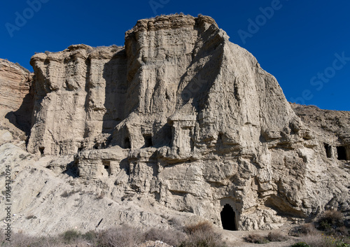 Canvas-taulu Eroded cliff with troglodyte caves under blue sky, Arguedas
