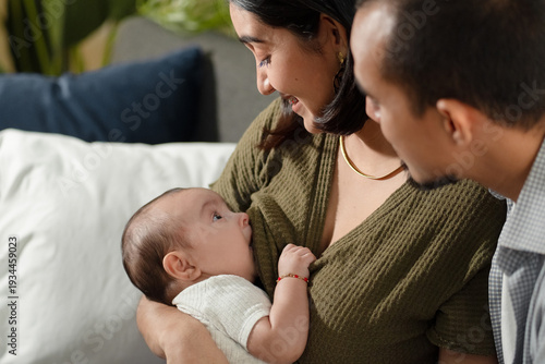 Mother breastfeeding baby with father looking on