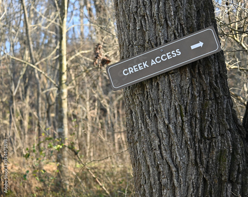 Creek access sign with arrow on a tree trunk in the woods