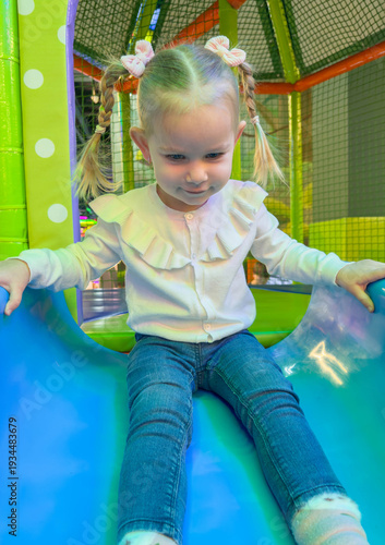 Little girl with pigtails sliding down a blue slide in a kids play center