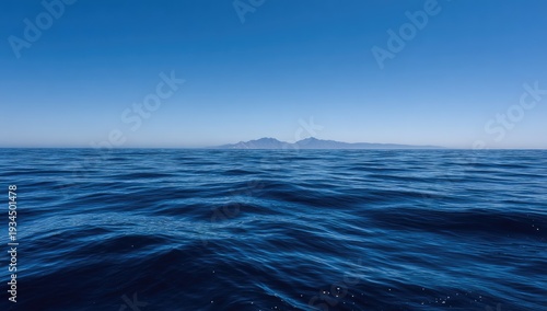 Open water view of dark blue sea, small mountainous island silhouettes against clear blue sky