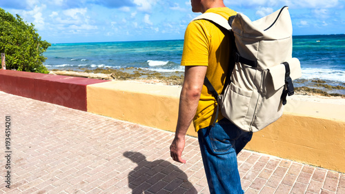 Man walking along ocean path with backpack